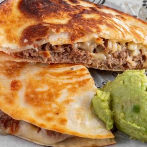 A Paco's Tacos quesadilla, cut in half, revealing melted cheese and meat, served with guacamole.