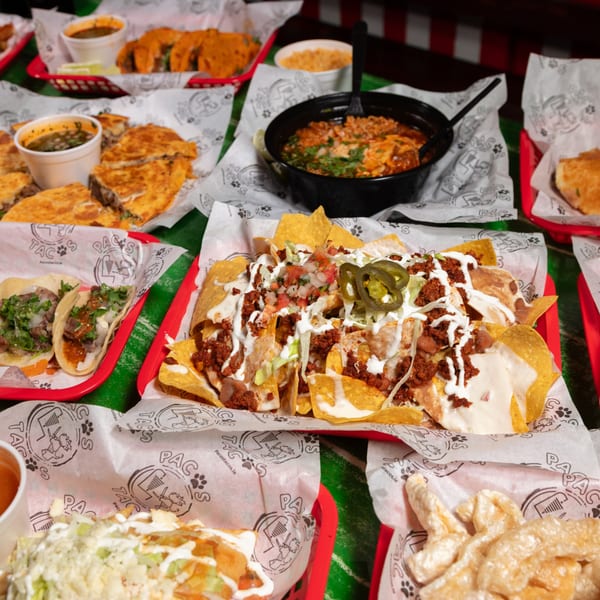 A vibrant spread of Pacos Tacos dishes, including nachos, tacos, quesadillas, and soup.