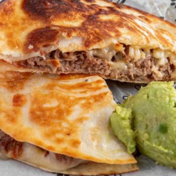 A Paco's Tacos quesadilla, cut in half, revealing melted cheese and shredded meat, with guacamole.