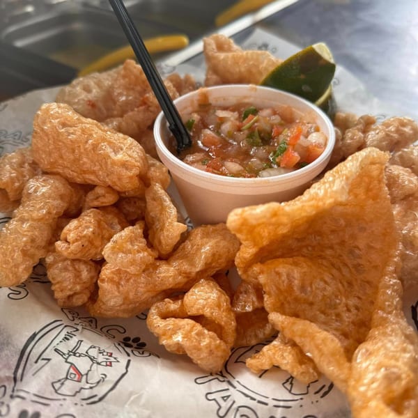 Crispy chicharrones with a side of fresh salsa and a lime wedge on Paco's Tacos branded paper.